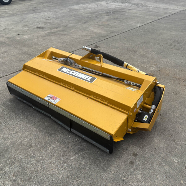Yellow McConnel mower attachment resting on a concrete surface, with hydraulic hoses and safety decals visible.