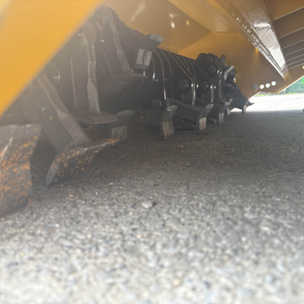 Low-angle close-up of the undercarriage of a yellow construction machine, showing black track links on asphalt ground