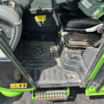 Interior of a green vehicle cab showing the entry area, with a yellow safety warning sticker and a textured step.