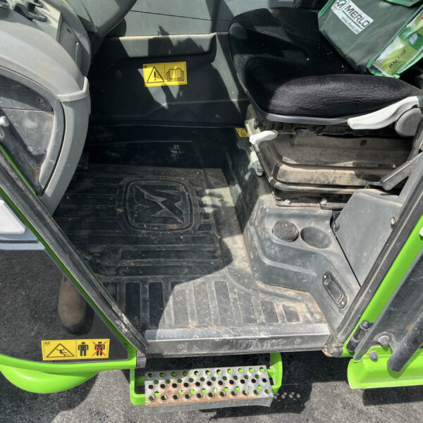 Interior of a green vehicle cab showing the entry area, with a yellow safety warning sticker and a textured step.