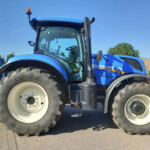 Close-up of a blue New Holland tractor front wheel and cabin at a dealership lot of farming equipment