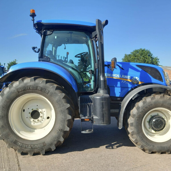 Close-up of a blue New Holland tractor front wheel and cabin at a dealership lot of farming equipment