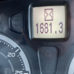 Close-up of a car dashboard: stop button on the left and a digital screen showing 681.3 with an hourglass icon.