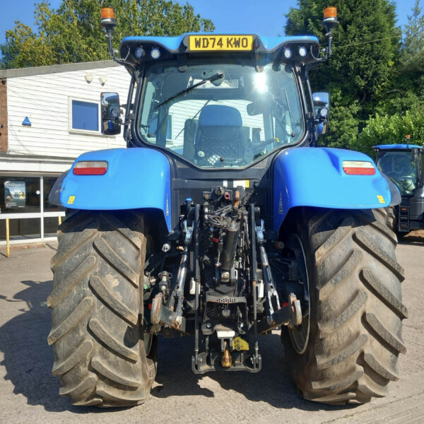 Front view of a large blue agricultural tractor with oversized rear tires parked outside a service shop.
