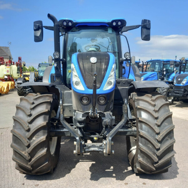 Front view of a large blue tractor with oversized treads parked in a lot, other blue tractors lined up in the background.