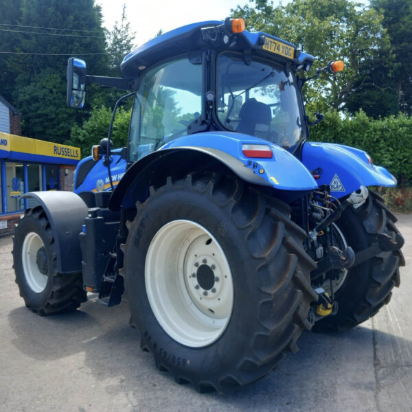 Blue New Holland tractor with large front wheel close up, parked outside an agriculture shop named 'Russells'