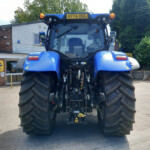 Rear view of a large blue tractor with oversized tires parked in a farm equipment service yard