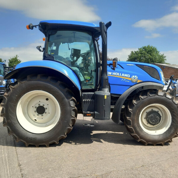 Blue New Holland tractor with oversized tires parked outdoors, service sign in background