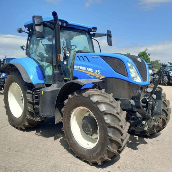 Blue New Holland tractor front view in a dealership lot, with large tires and other blue tractors visible in the background.