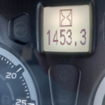 Close-up of a car dashboard showing a digital timer with an hourglass icon and the value 1453.3. Nearby is the STOP button on the steering console.