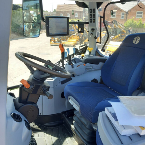 Interior of a blue tractor cabin with steering wheel, multiple control levers, and a mounted touchscreen monitor facing the operator