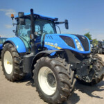 Blue New Holland tractor in a row on a sunny outdoor lot, foreground showing model T7.260 and large white wheels