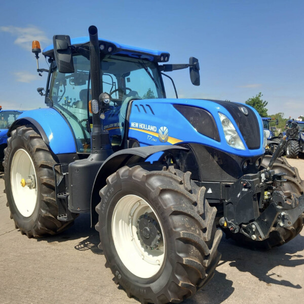 Blue New Holland tractor in a row on a sunny outdoor lot, foreground showing model T7.260 and large white wheels