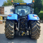 Rear view of a blue New Holland tractor with large tires parked outside a service building (New Holland Agriculture Service).