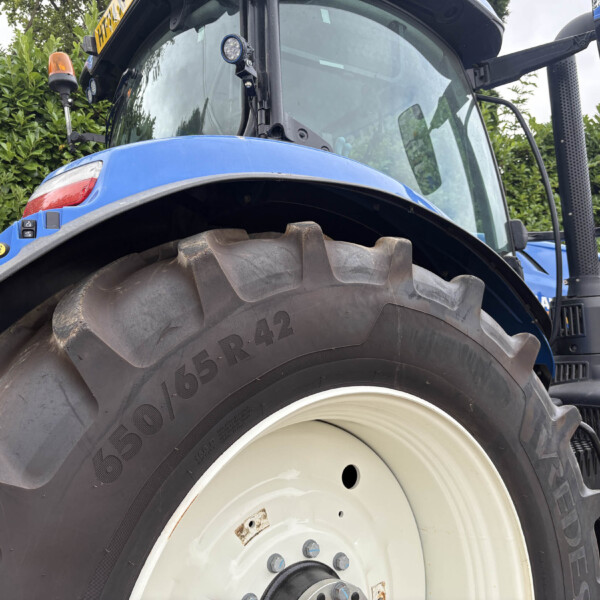 Close-up of a blue agricultural tractor front wheel with a large treaded tire and part of the cab in the background.