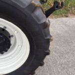 Close-up of a large tractor tire and white rim, with dirt on the tread and bolts around the hub on a paved surface.