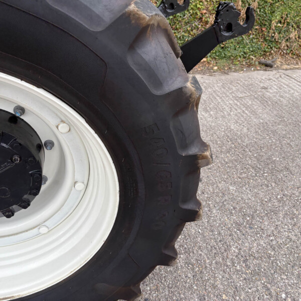 Close-up of a large tractor tire and white rim, with dirt on the tread and bolts around the hub on a paved surface.