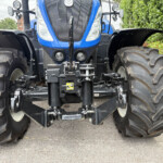 Front view of a blue New Holland tractor facing the camera with oversized rear tires and front hitch components behind it.
