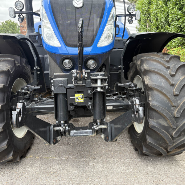 Front view of a blue New Holland tractor facing the camera with oversized rear tires and front hitch components behind it.