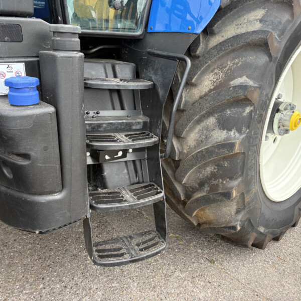 Close-up of a large tractor wheel with muddy tread, blue body panel, and black steps/foot rail near the cab.