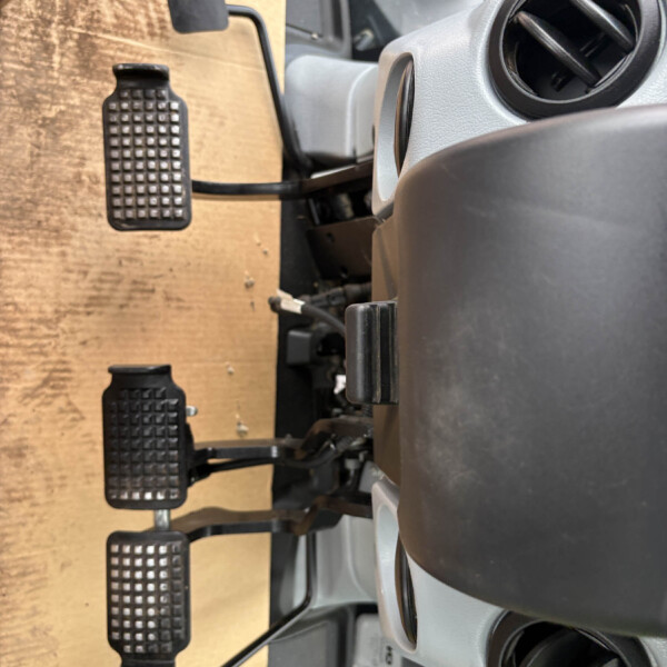 Close-up of vehicle interior showing textured brake/clutch pedals and part of the center console with a cup holder on the right.