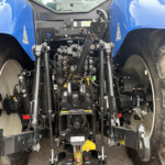 Rear view of a blue tractor showing the three-point hitch hydraulics, controls, and hitch arms with large rear tires on either side.