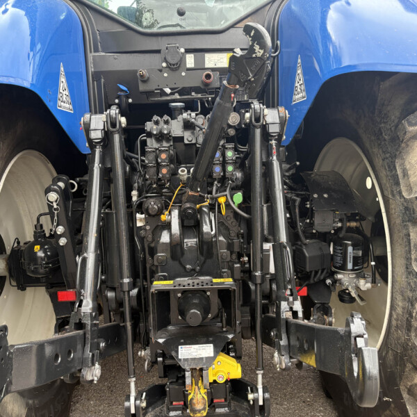 Rear view of a blue tractor showing the three-point hitch hydraulics, controls, and hitch arms with large rear tires on either side.