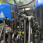 Close-up of the hydraulic control levers and connectors inside a blue tractor cab, with warning labels visible on the panel.