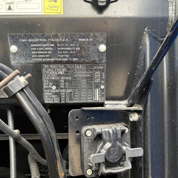 Close-up of a machine identification plate with CNH INDUSTRIAL ITALIA S.P.A. text and specs, on a dusty black surface of a vehicle or equipment panel