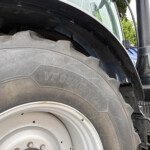 Close-up of a large tractor rear tire and wheel, with a black fender and blue tractor body nearby.