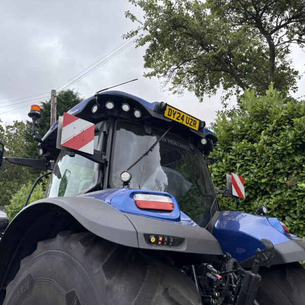 Front of a blue tractor with an orange beacon, red-and-white reflective panel, and license plate DY24 UZR.