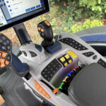 Inside the cab of a modern tractor showing a joystick, control panels, and a touchscreen display on the dashboard