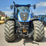 Front view of a large blue tractor with oversized tires parked in a lot of farm machinery.