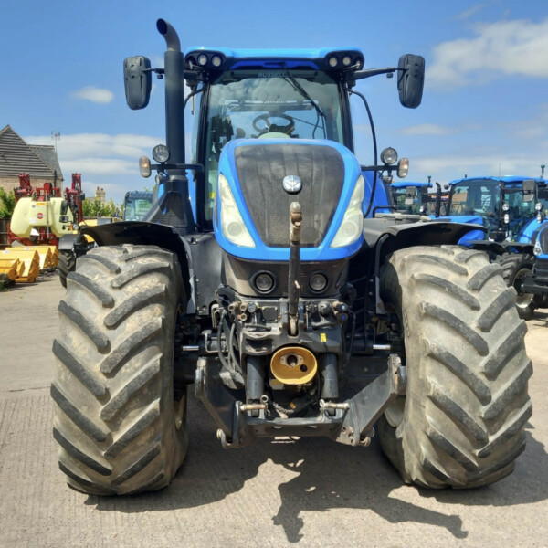 Front view of a large blue tractor with oversized tires parked in a lot of farm machinery.