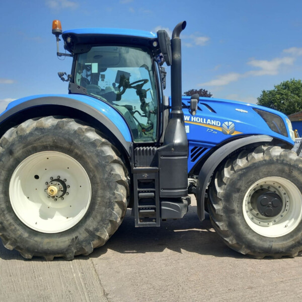 Close-up of a bright blue New Holland tractor showing large front tire, cab, and steps on a dealership lot.