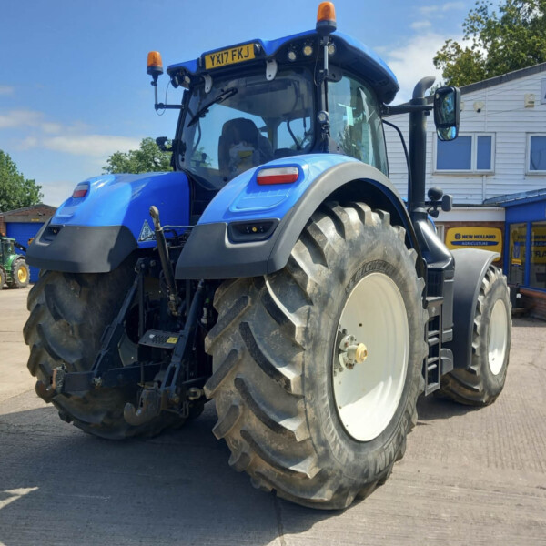 Close-up view of a blue agricultural tractor with oversized rear tire, parked outside a dealership.