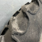 Close-up of a muddy work boot sole with dirt and debris packed in the tread.