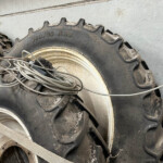 Large, muddy tractor tires with deep treads in a dusty storage area, with tangled wires on the rims