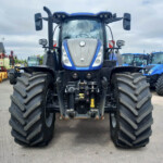 Front view of a large blue tractor with oversized tires, parked in a lot with other agricultural machinery behind it