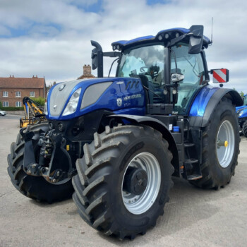 Blue New Holland tractor on a dealership lot, front-left view with oversized tires.