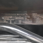 Close-up of a metal vehicle data plate under the hood showing manufacturer name (New Holland) and technical specifications such as weight and mass values (in kg).