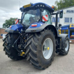Blue New Holland agricultural tractor on a dealership lot in front of a Russell's shop, large tires and front cab visible.
