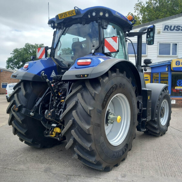 Blue New Holland agricultural tractor on a dealership lot in front of a Russell's shop, large tires and front cab visible.