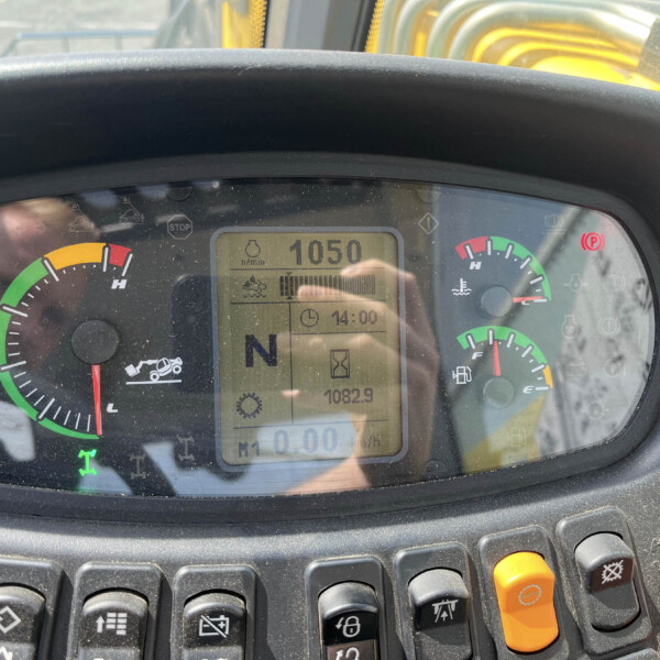 Close-up of a vehicle dashboard (tractor) with circular gauges, digital display showing 1050 rpm and various indicator icons, and control buttons below