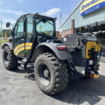 New Holland agricultural loader parked outside a dealership, showing large tires and glass cab under a clear blue sky.