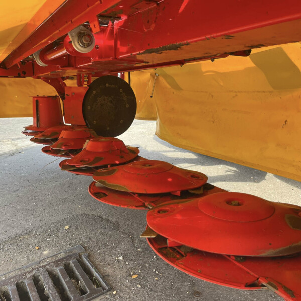 Close-up of red disc blades attached to a yellow farming machine, resting on pavement.