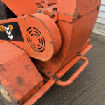 Close-up of an orange construction compactor with a black POWER logo and vent, showing worn paint.
