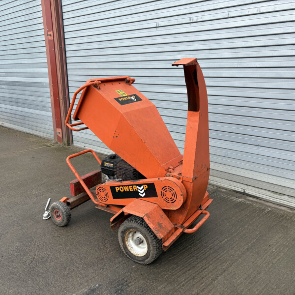 Orange mobile wood chipper/shredder on wheels beside a corrugated metal door, ready for use in a yard.
