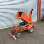 Orange industrial lift parked beside a grey corrugated metal shutter.