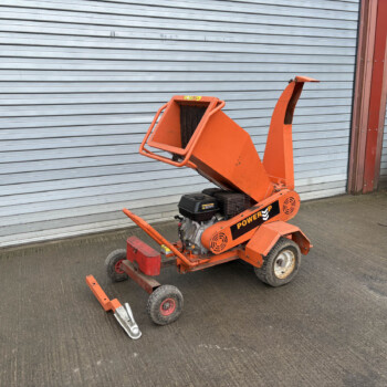 Orange mobile construction lift with an extended arm resting on the ground in front of a gray corrugated metal shutter.